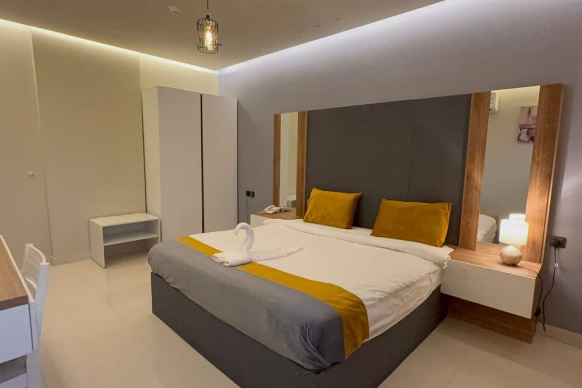 Une chambre d’hôtel moderne équipée d’un grand lit, d’une table de chevet, d’une commode, d’un bureau et d’un miroir.
