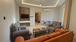 A modern living room with grey and orange sofas, a coffee table, and a flat-screen TV mounted on the wall. - Lamar Park Hotel Al Rayan (Tabuk)