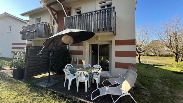 A two-story house with a balcony, outdoor seating area with chairs and a table, and a small garden. - House in Soulac-sur-mer Near Beach (Soulac-sur-Mer)
