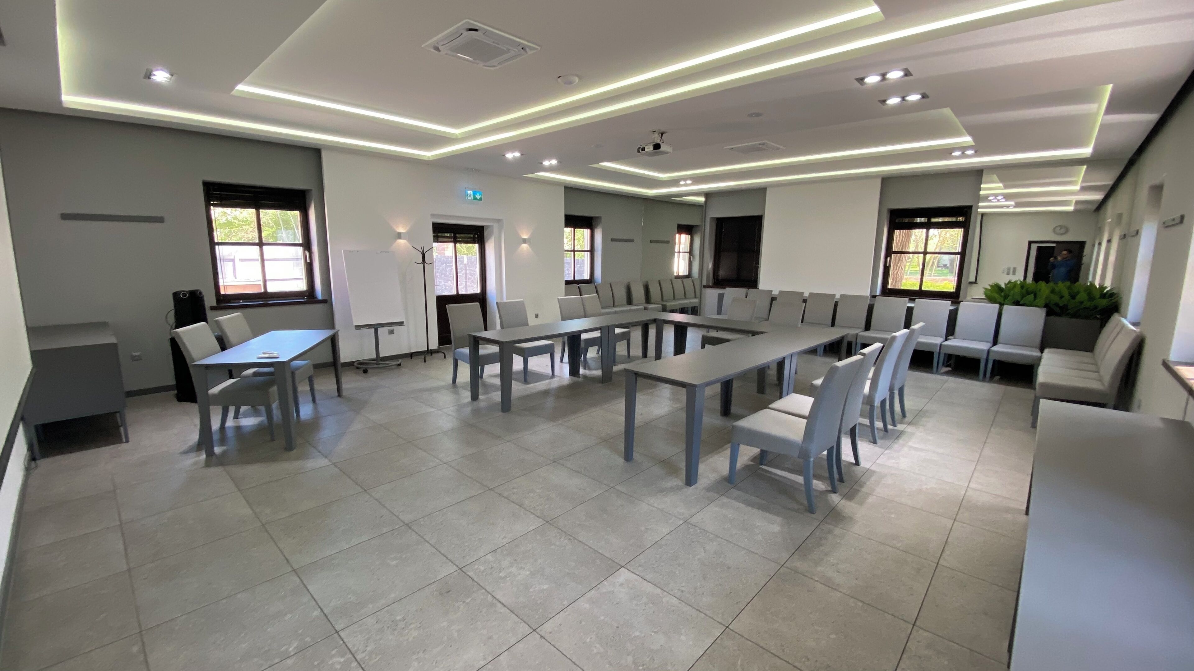 Uma sala de conferência moderna com várias mesas e cadeiras, um quadro branco e um projetor.