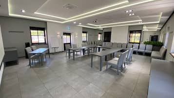 Una sala de conferencias moderna con varias mesas y sillas, una pizarra y un proyector.