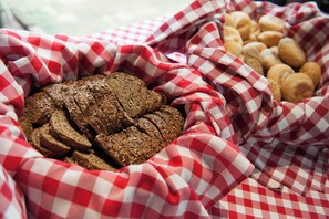 En korg med skivad bröd och småbröd på ett rött och vitt rutigt tyg.