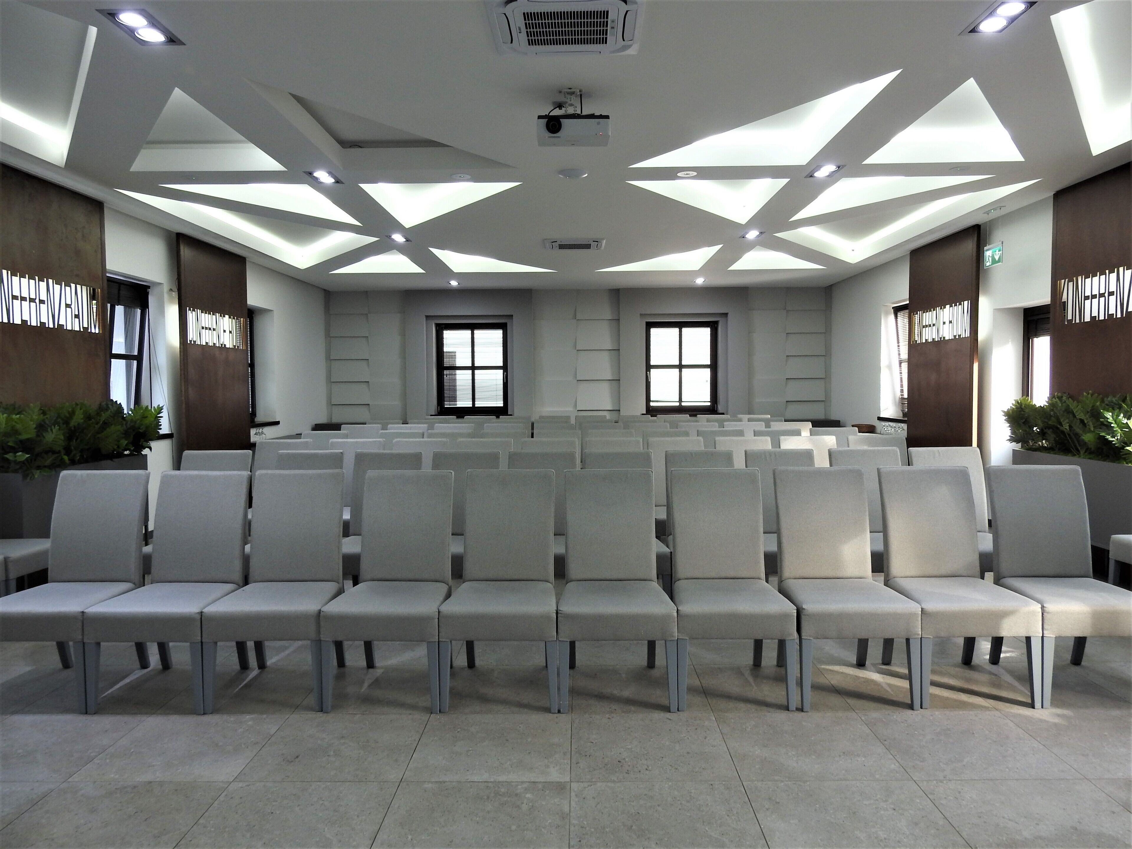 Un salón de conferencias con filas de sillas, un proyector y un ventanal grande.
