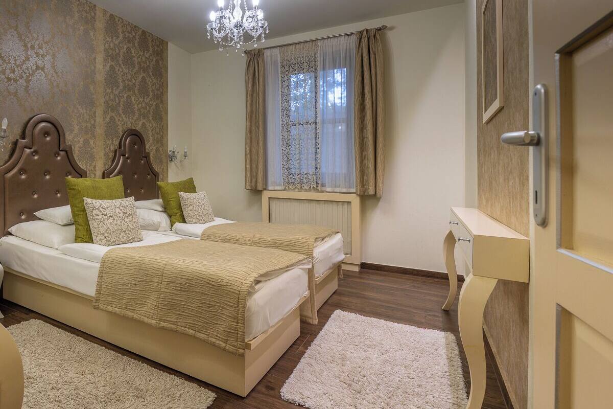 A bedroom with two beds, a chandelier, a window with curtains, and a wooden door.