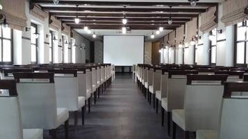 Une salle de conférence avec des rangées de chaises disposées face à un grand écran situé au fond de la pièce.