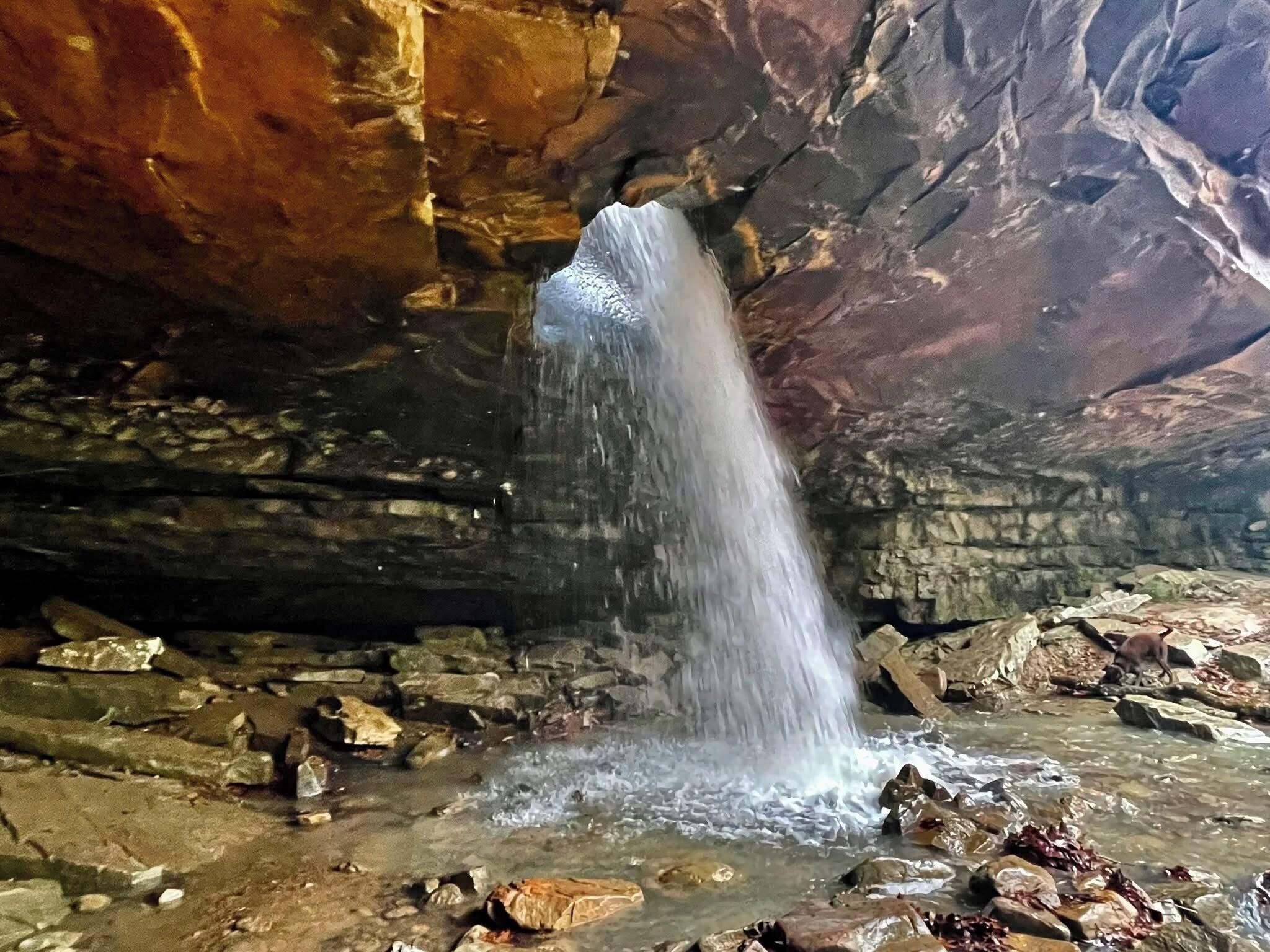 Une grotte avec une cascade et un terrain rocheux.
