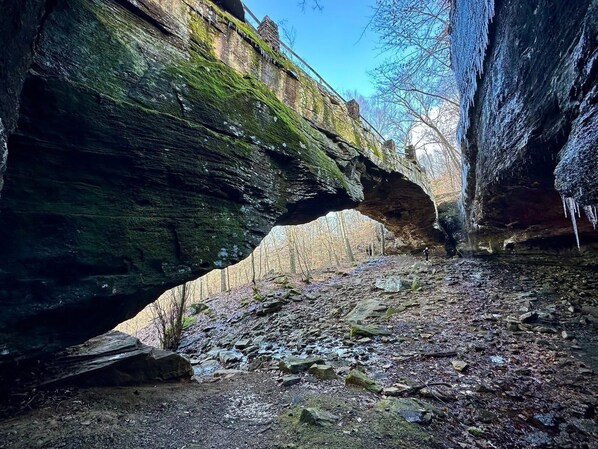 A natural rock arch formation with a forested area beneath.