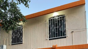 A two-story building with a beige exterior, orange trim, and barred windows. - Casa Vacacional Canoa 138 (La Paz)