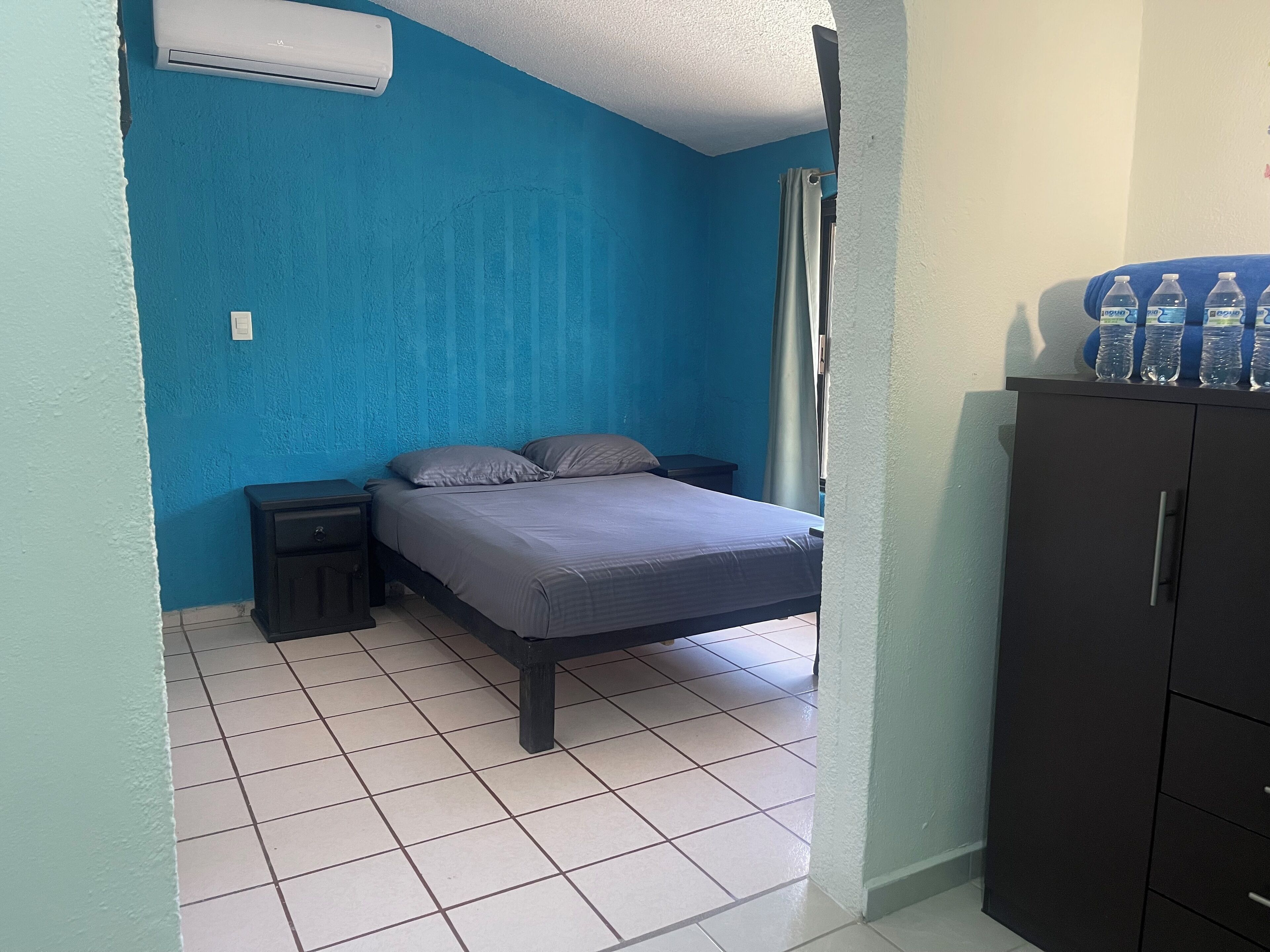 Een kamer met een bed, nachtkastje, kast en een waterdispenser.