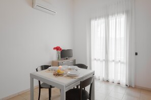 Un comedor con una mesa dispuesta para dos personas, un televisor y una ventana con cortinas translúcidas.