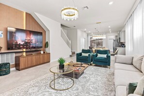 Ein modernes Wohnzimmer mit Flachbildfernseher, einer Holzunterhaltungsecke, einem Glastisch und einer Couch.