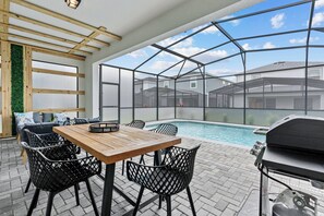 Eine Terrasse im Freien mit Holztisch und -stühlen, einem Grill und einem Pool.