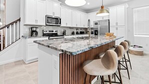 Una cocina moderna con armarios blancos, encimera de granito y una isla central con taburetes de bar.