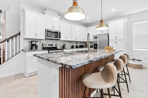 A modern kitchen with white cabinets, a granite countertop, and a central island with bar stools. - 6BR house with pool near Disney area (Kissimmee)