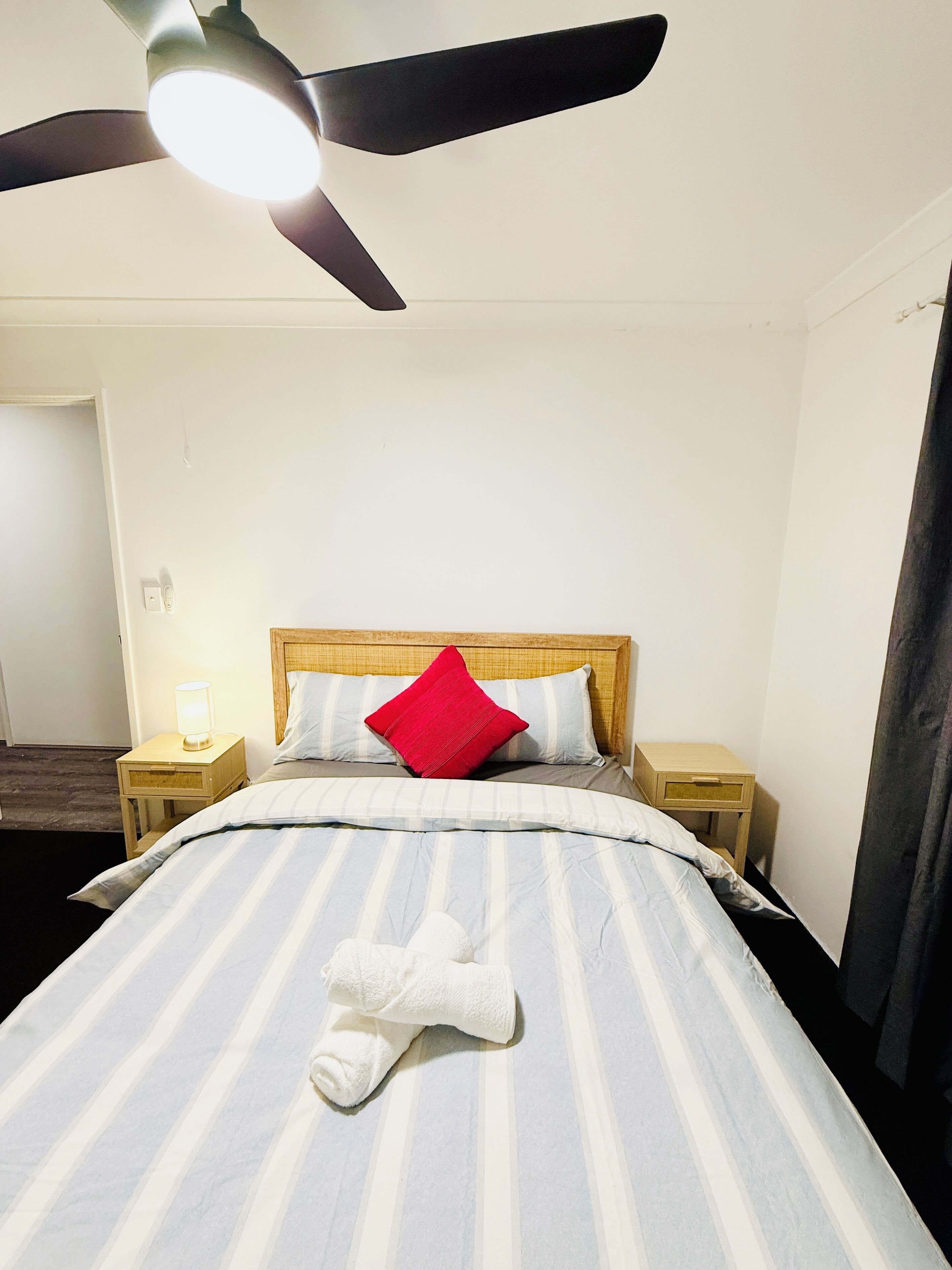 Een hotelkamer met een bed, een plafondventilator, een nachtkastje met een lamp en een houten hoofdbord.