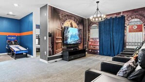 Ein Zimmer mit Flachbildfernseher, einem Spieltisch, einer Couch und Wandgemälde.