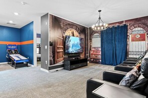 Ein Zimmer mit Flachbildfernseher, einem Spieltisch, einer Couch und Wandgemälde.