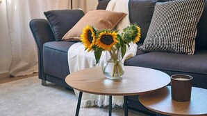 A living room with a dark grey sofa, a round wooden coffee table with a vase of sunflowers, and a floor lamp. - Cosima - Kaiserslautern (Kaiserslautern)