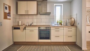 A compact kitchen with a dishwasher, oven, and a window providing natural light. - Cosima - Kaiserslautern (Kaiserslautern)
