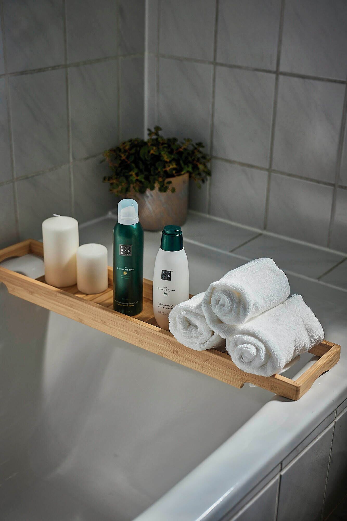 A bathroom with a wooden tray holding toiletries, a potted plant, and rolled towels on a white countertop.