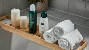 A bathroom with a wooden tray holding toiletries, a potted plant, and rolled towels on a white countertop.