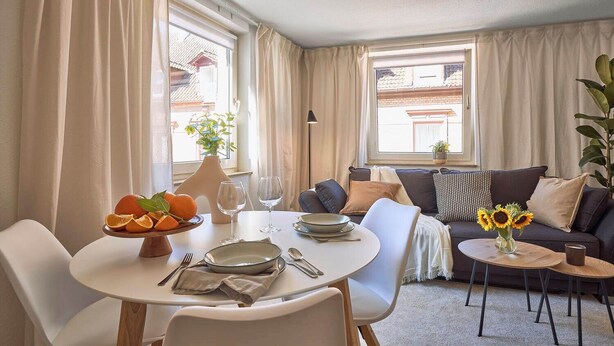 A dining area with a round table, chairs, a bowl of fruit, and a vase of sunflowers. - Cosima - Kaiserslautern (Kaiserslautern)