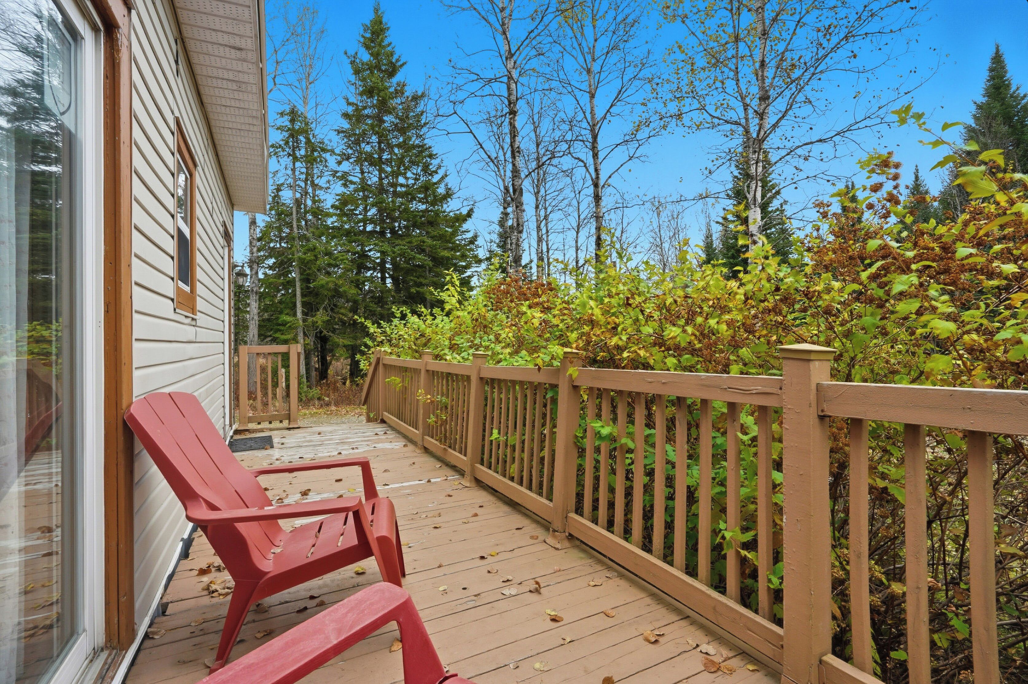 Une terrasse en bois avec des chaises rouges, une balustrade en bois et une vue sur les arbres et le feuillage.
