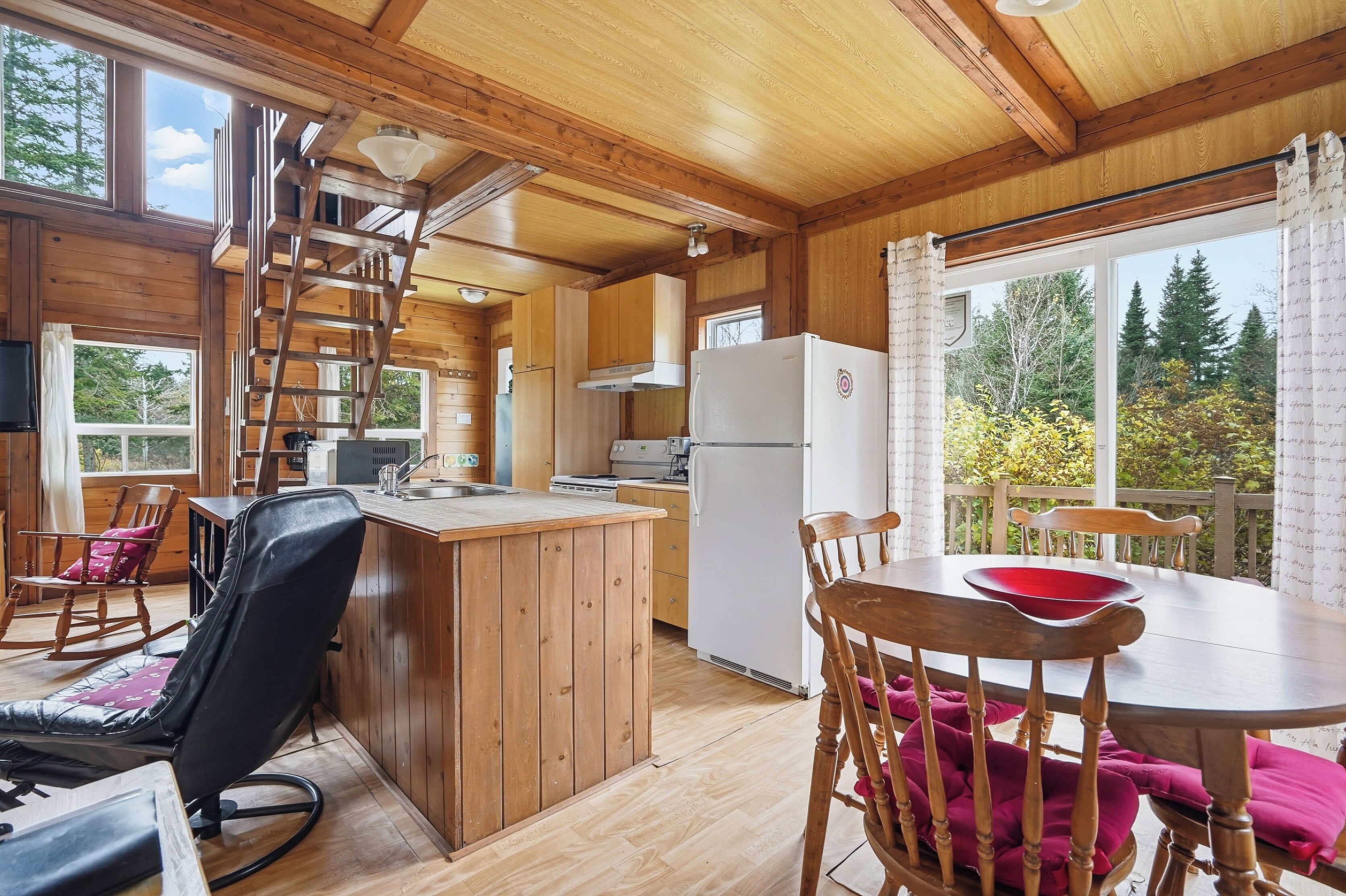 Een houten blokhut van binnen met een keuken, eethoek en balkon met uitzicht op bomen.