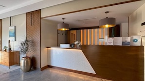 A reception area with a wooden reception desk, two pendant lights, a potted plant, and a wooden cabinet. - DIFFERENT HOTEL (Tabuk)
