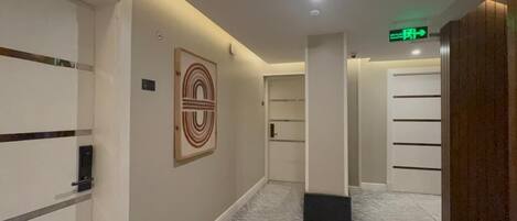 A hallway with a marble floor, a framed artwork on the wall, and a door with a handle.