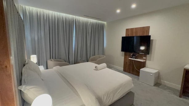 A modern hotel room with a large bed, two armchairs, a flat-screen TV, and a small bedside table. - DIFFERENT HOTEL (Tabuk)