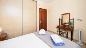 A hotel room with a bed, a desk, a mirror, a wardrobe, and a standing heater.