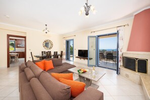 A modern living room with a sofa, a dining area, a TV, and a fireplace.