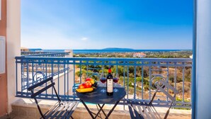 Ein Balkon mit Tisch, einer Weinflasche und einem Glas mit Blick auf eine Küstenlandschaft.