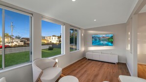 Un salon moderne avec de grandes fenêtres, un radiateur blanc et un téléviseur fixé au mur.