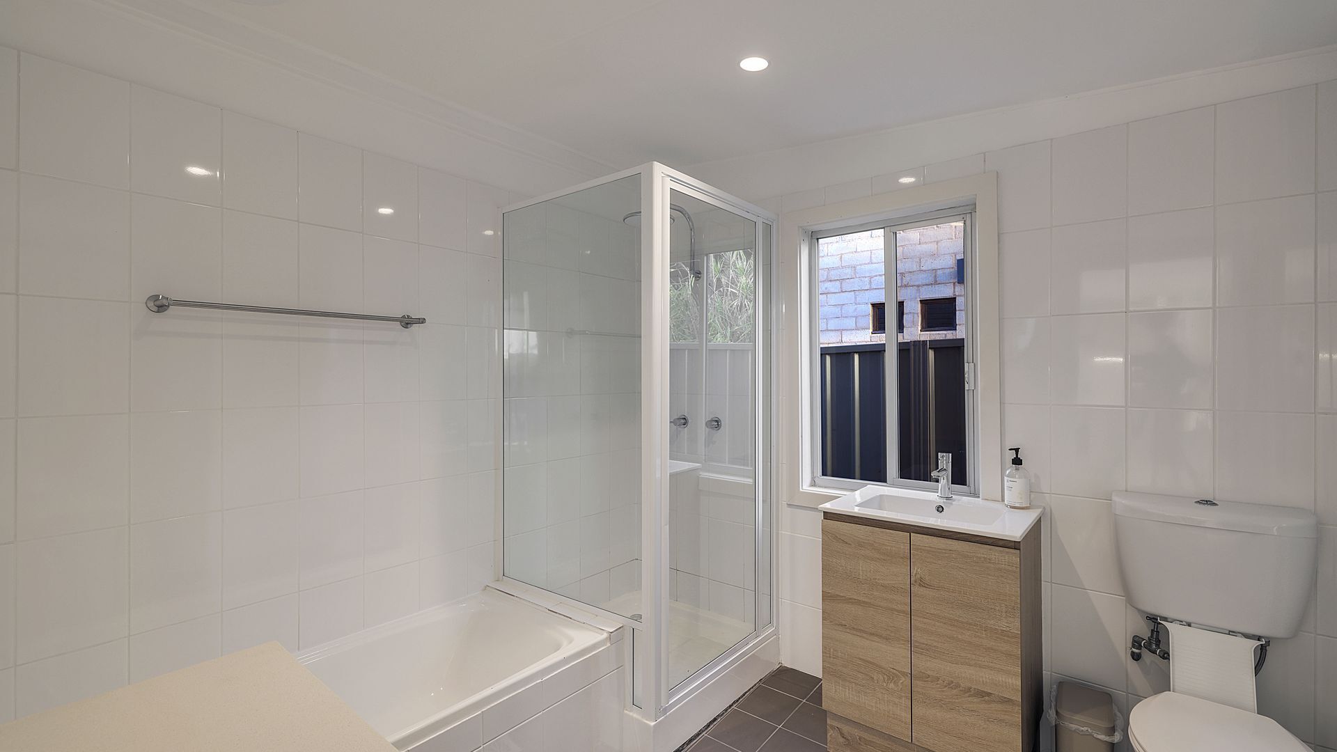 Un baño moderno con ducha envuelta en vidrio, una bañera, un lavamanos con ventana y un inodoro.