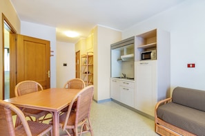 A compact kitchen with a microwave, a dining table with wicker chairs, and a sofa. - Chic Rina Sea 1 Bedroom Apt B4 Sleeps 4 Person (Alghero)