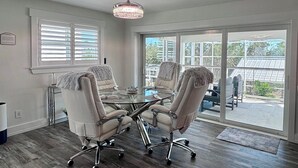 A conference room with a glass table and four chairs, large windows with blinds, and a chandelier. - Tropical Hideaway - Three Bedroom House, Sleeps 8 (Fort Myers Beach)
