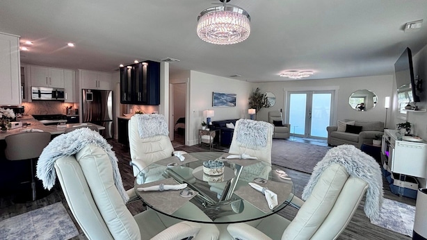 A modern living room with a glass coffee table, white leather chairs, and a chandelier. - Tropical Hideaway - Three Bedroom House, Sleeps 8 (Fort Myers Beach)