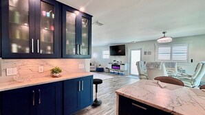 A modern kitchen with dark blue cabinets, a marble countertop, and a dining area with a table and chairs. - Tropical Hideaway - Three Bedroom House, Sleeps 8 (Fort Myers Beach)