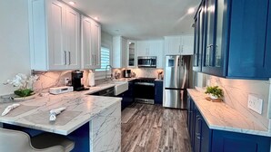 A modern kitchen with white and blue cabinets, a marble countertop, stainless steel appliances, and a wooden floor. - Tropical Hideaway - Three Bedroom House, Sleeps 8 (Fort Myers Beach)