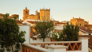 A historic building with a bell tower, surrounded by trees and other buildings. - Casa Pizarro Hotel (Cáceres)