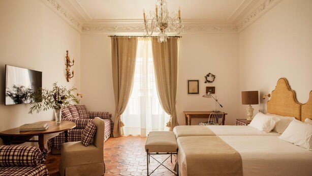 A hotel room with a checkered sofa, a small table, a desk, a bed, and a chandelier. - Casa Pizarro Hotel (Cáceres)