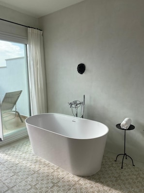A modern bathroom with a freestanding bathtub, a glass shower enclosure, and a small table with a towel. - Casa Pizarro Hotel (Cáceres)