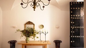 A room with a wooden table, a mirror, a vase with greenery, a candelabra, two black metal chairs, and a black door with rivets. - Casa Pizarro Hotel (Cáceres)