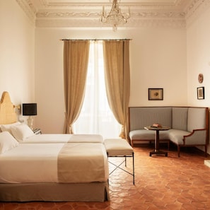 A hotel room with a large bed, a sofa, a small table, and a chandelier. - Casa Pizarro Hotel (Cáceres)