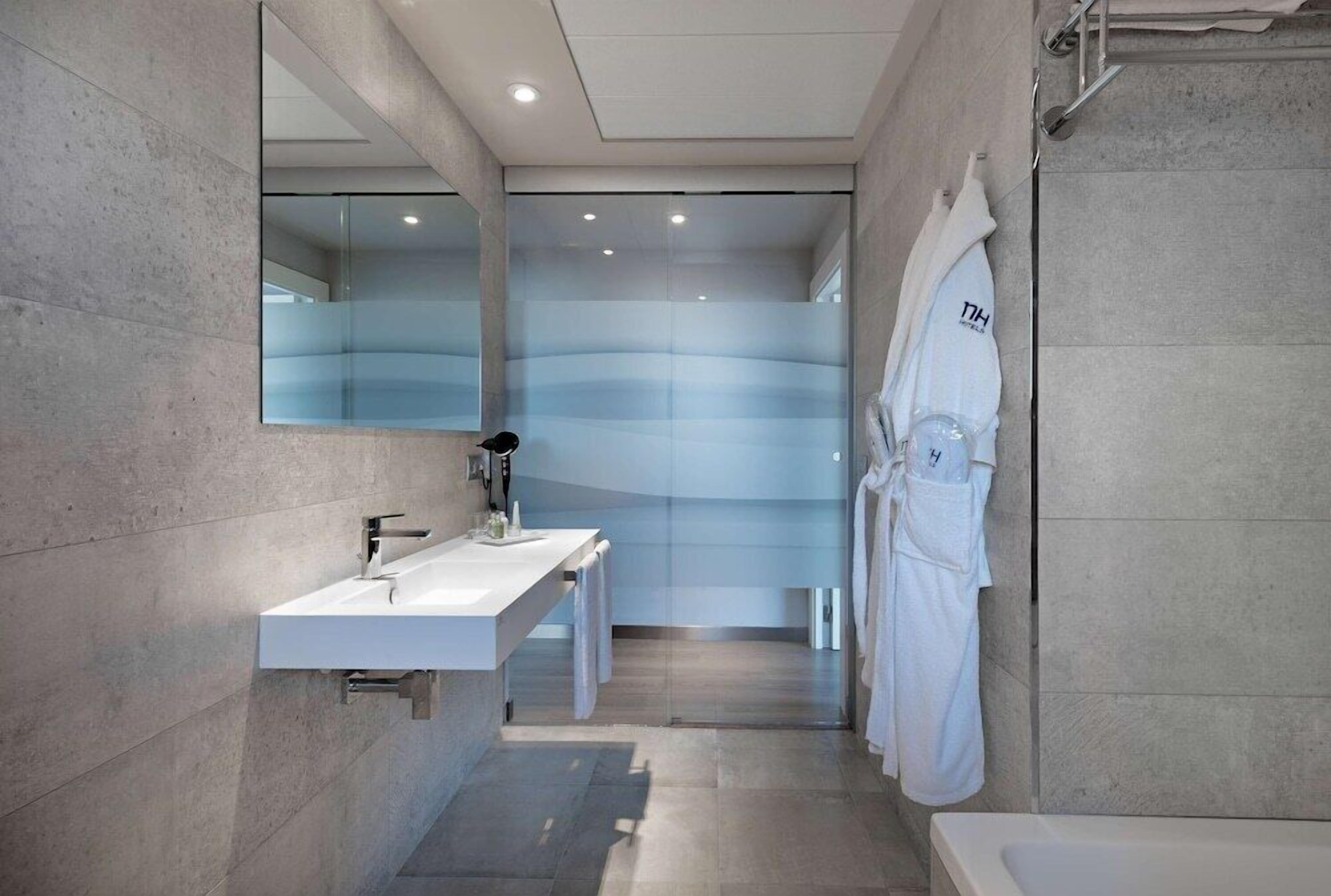 A modern bathroom with a large mirror, two sinks, a shower area, and a bathtub.