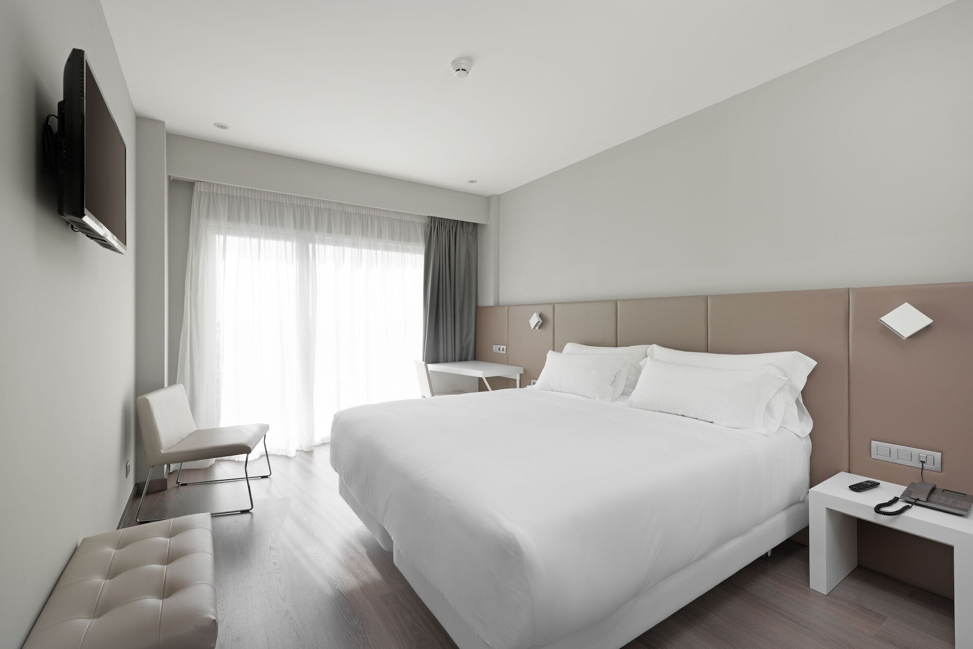 Una habitación de hotel moderna con una cama grande, un escritorio, una silla y un televisor montado en la pared.