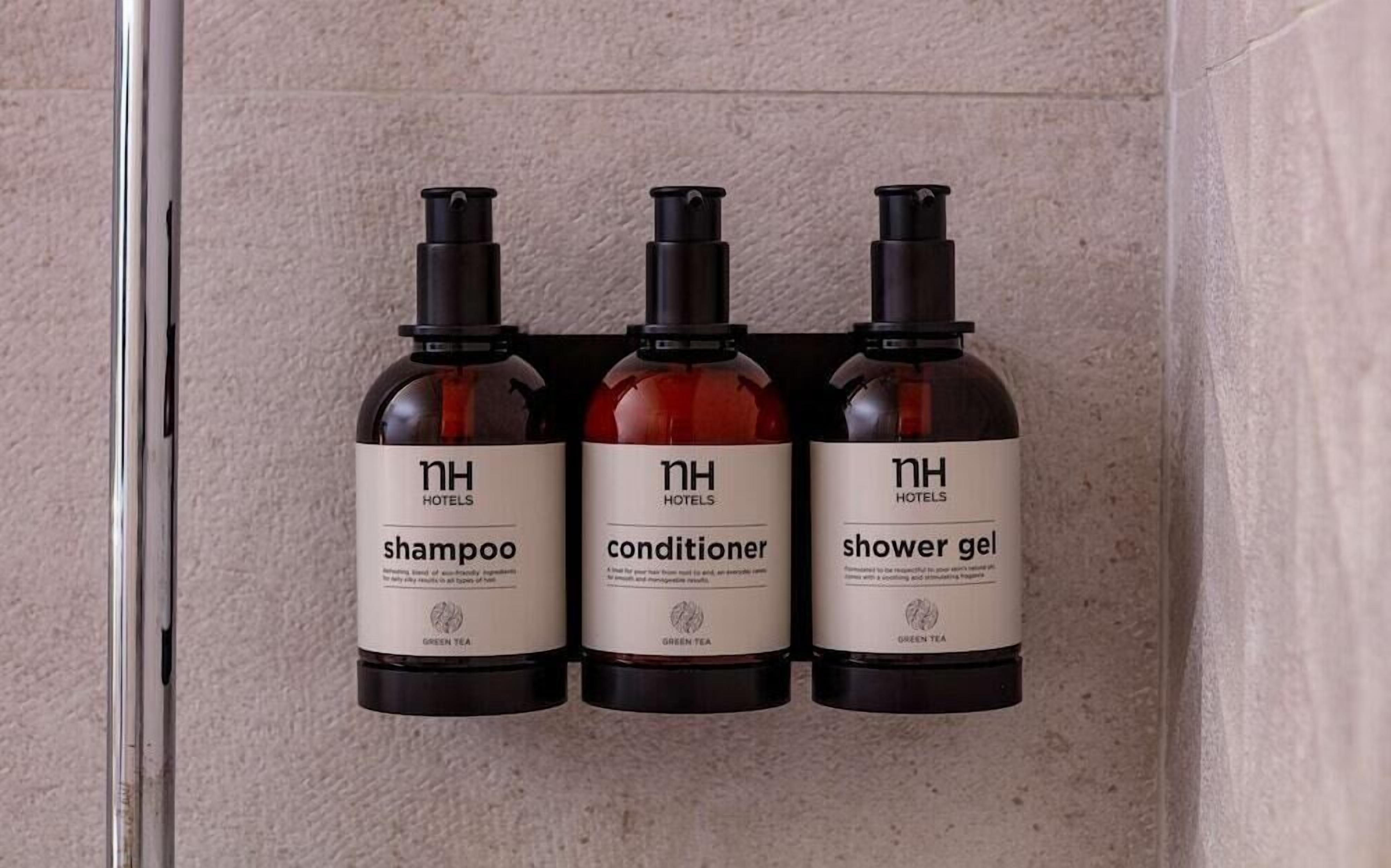 Drei Hotelzimmer-Annehmlichkeiten: Shampoo, Conditioner und Duschgel, beschriftet mit 'NH Hotels' und 'GRÜNER TEE'.