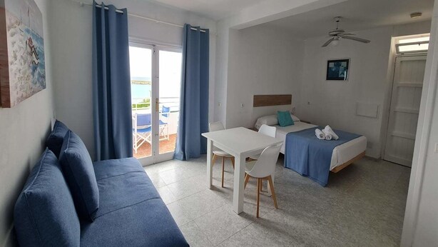 A room with a bed, a sofa, a table, and a ceiling fan. - Vistamar Apartments (Es Migjorn Gran)